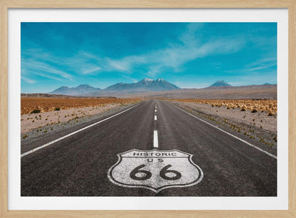 A framed photograph of the iconic Historic US Route 66 shield painted on a long, straight asphalt road that stretches through a desert landscape toward distant snow-capped mountains under a vibrant blue sky. Wall Art