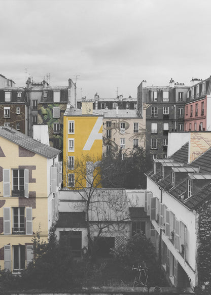 A framed, vertical photograph with selective color, showing a dense cluster of Parisian-style buildings under an overcast sky. Most of the image is in black and white, but one building is a vibrant yellow with a large white 'A' painted on it, creating a striking focal point. Wall Art