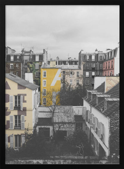 A framed, vertical photograph with selective color, showing a dense cluster of Parisian-style buildings under an overcast sky. Most of the image is in black and white, but one building is a vibrant yellow with a large white 'A' painted on it, creating a striking focal point. Wall Art