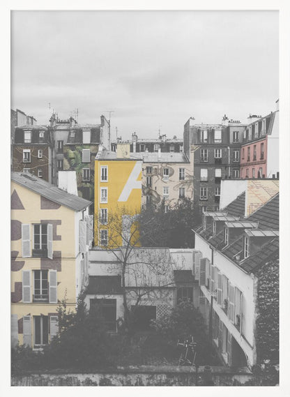 A framed, vertical photograph with selective color, showing a dense cluster of Parisian-style buildings under an overcast sky. Most of the image is in black and white, but one building is a vibrant yellow with a large white 'A' painted on it, creating a striking focal point. Wall Art