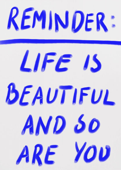 A framed poster featuring a positive affirmation handwritten in a blue, brush-stroke style font on a white background. The text reads 'REMINDER: LIFE IS BEAUTIFUL AND SO ARE YOU', with a blue line separating 'REMINDER:' from the rest of the quote. Print