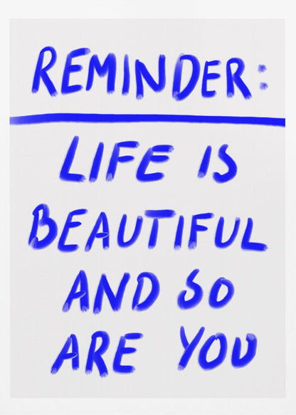 A framed poster featuring a positive affirmation handwritten in a blue, brush-stroke style font on a white background. The text reads 'REMINDER: LIFE IS BEAUTIFUL AND SO ARE YOU', with a blue line separating 'REMINDER:' from the rest of the quote. Print