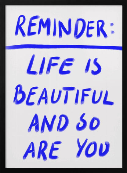 A framed poster featuring a positive affirmation handwritten in a blue, brush-stroke style font on a white background. The text reads 'REMINDER: LIFE IS BEAUTIFUL AND SO ARE YOU', with a blue line separating 'REMINDER:' from the rest of the quote. Print