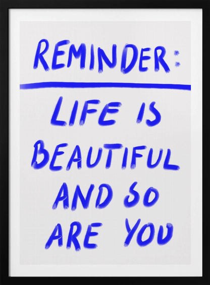 A framed poster featuring a positive affirmation handwritten in a blue, brush-stroke style font on a white background. The text reads 'REMINDER: LIFE IS BEAUTIFUL AND SO ARE YOU', with a blue line separating 'REMINDER:' from the rest of the quote. Print