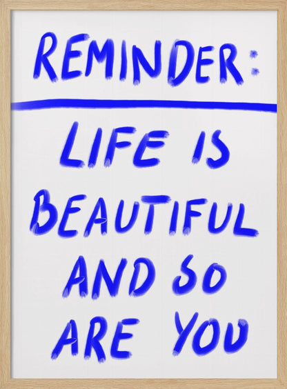 A framed poster featuring a positive affirmation handwritten in a blue, brush-stroke style font on a white background. The text reads 'REMINDER: LIFE IS BEAUTIFUL AND SO ARE YOU', with a blue line separating 'REMINDER:' from the rest of the quote. Print