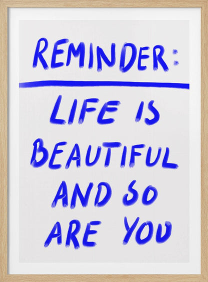 A framed poster featuring a positive affirmation handwritten in a blue, brush-stroke style font on a white background. The text reads 'REMINDER: LIFE IS BEAUTIFUL AND SO ARE YOU', with a blue line separating 'REMINDER:' from the rest of the quote. Print
