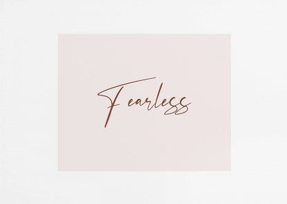 A framed artwork featuring the word 'Fearless' in a flowing brown script font on a pale pink background. The piece is surrounded by a white mat and a textured silver frame. Wall Art