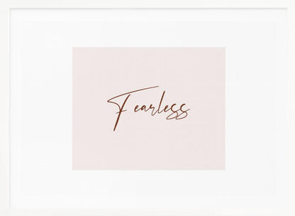 A framed artwork featuring the word 'Fearless' in a flowing brown script font on a pale pink background. The piece is surrounded by a white mat and a textured silver frame. Wall Art