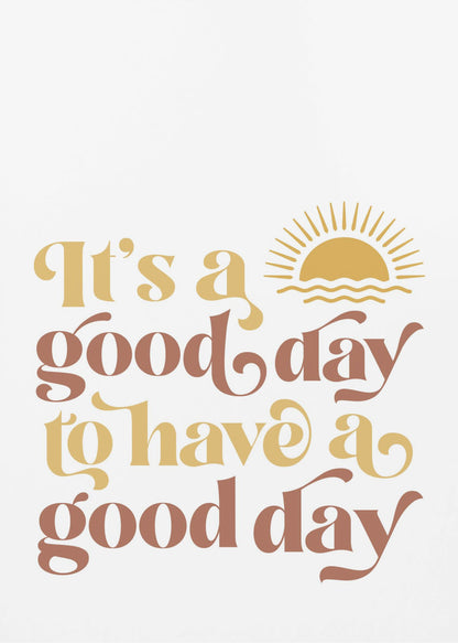 A framed art print with a white background featuring the quote 'It's a good day to have a good day' in a retro, curvy font. The text color alternates between terracotta brown and mustard yellow. Above the text is a small yellow icon of a sun rising over waves. Wall Art