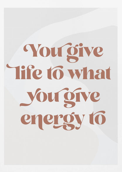 A framed motivational poster featuring the quote 'You give life to what you give energy to'. The text is printed in a dusty rose color using a stylish, retro serif font on a light gray background with subtle wavy shapes. Poster