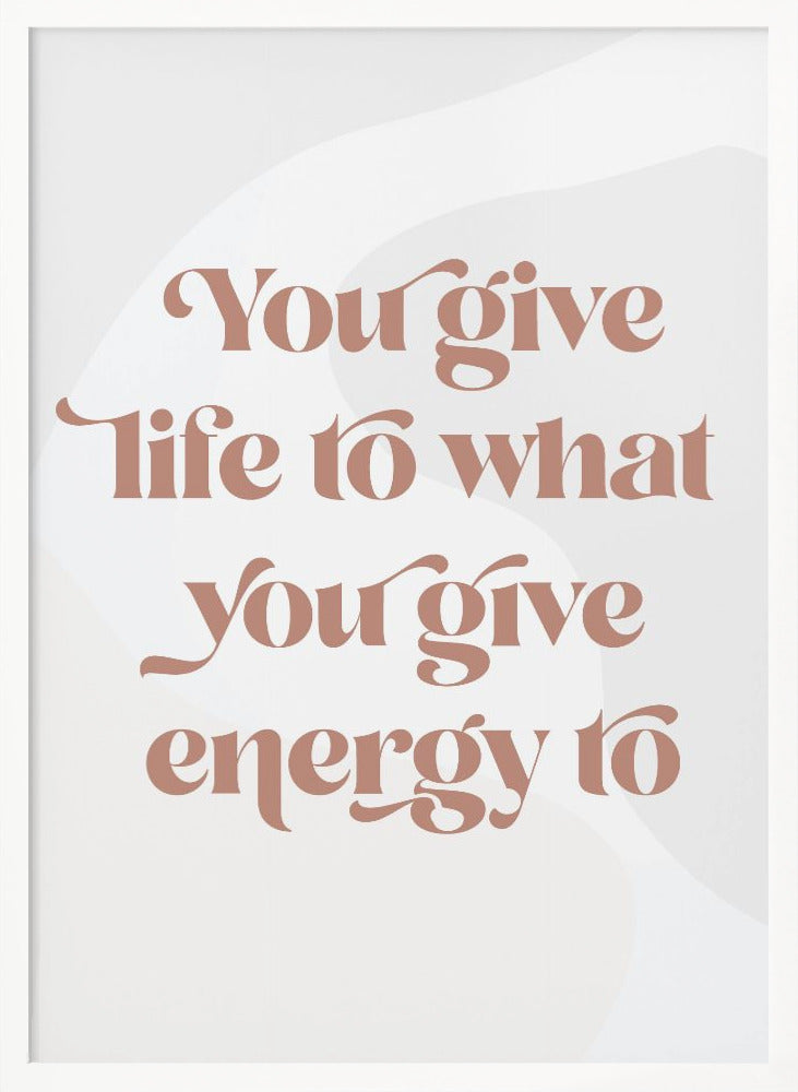 A framed motivational poster featuring the quote 'You give life to what you give energy to'. The text is printed in a dusty rose color using a stylish, retro serif font on a light gray background with subtle wavy shapes. Poster
