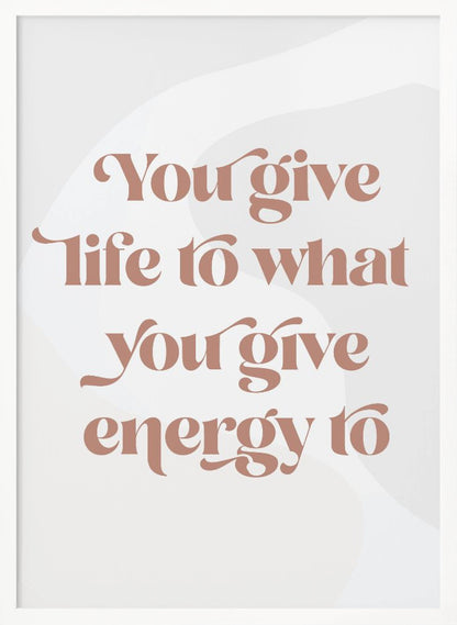 A framed motivational poster featuring the quote 'You give life to what you give energy to'. The text is printed in a dusty rose color using a stylish, retro serif font on a light gray background with subtle wavy shapes. Poster