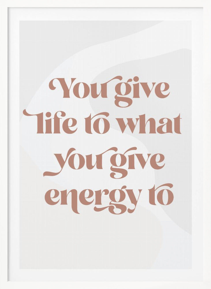 A framed motivational poster featuring the quote 'You give life to what you give energy to'. The text is printed in a dusty rose color using a stylish, retro serif font on a light gray background with subtle wavy shapes. Poster