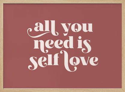 A framed art print with a dusty rose background. In the center, the phrase 'all you need is self love' is written in a creamy white, stylized, retro font. The artwork is enclosed in a simple silver frame. Decor