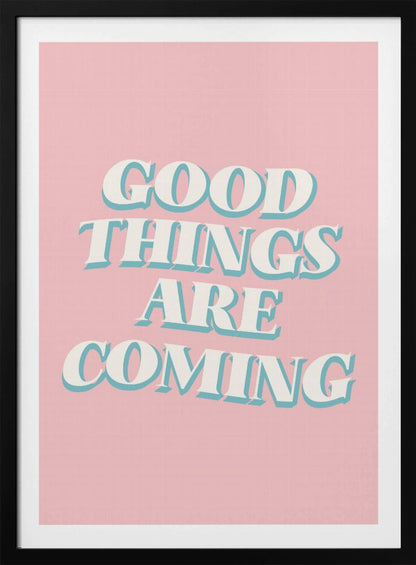 A framed poster with a light pink background featuring the motivational phrase 'GOOD THINGS ARE COMING'. The text is in a white, retro-style serif font with a light blue drop shadow, giving it a three-dimensional effect. Poster