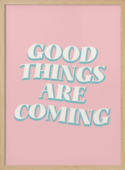 A framed poster with a light pink background featuring the motivational phrase 'GOOD THINGS ARE COMING'. The text is in a white, retro-style serif font with a light blue drop shadow, giving it a three-dimensional effect. Poster
