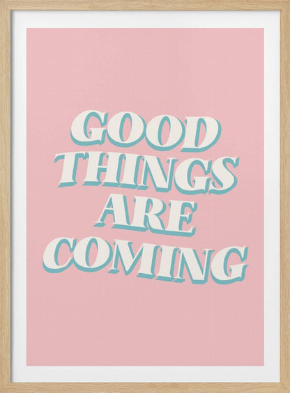 A framed poster with a light pink background featuring the motivational phrase 'GOOD THINGS ARE COMING'. The text is in a white, retro-style serif font with a light blue drop shadow, giving it a three-dimensional effect. Poster