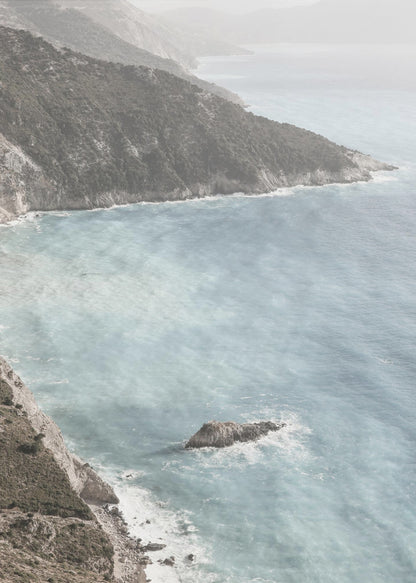 A high-angle photograph of a rugged, green coastline meeting a misty, light-blue ocean. The hazy atmosphere softens the view of the distant mountains and the waves crashing against the rocky shores. Poster