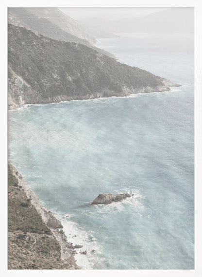 A high-angle photograph of a rugged, green coastline meeting a misty, light-blue ocean. The hazy atmosphere softens the view of the distant mountains and the waves crashing against the rocky shores. Poster