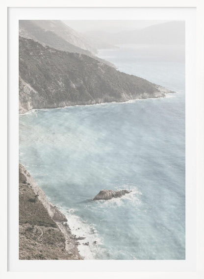 A high-angle photograph of a rugged, green coastline meeting a misty, light-blue ocean. The hazy atmosphere softens the view of the distant mountains and the waves crashing against the rocky shores. Poster