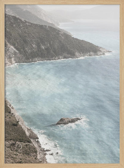 A high-angle photograph of a rugged, green coastline meeting a misty, light-blue ocean. The hazy atmosphere softens the view of the distant mountains and the waves crashing against the rocky shores. Poster