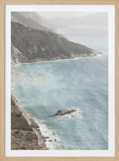 A high-angle photograph of a rugged, green coastline meeting a misty, light-blue ocean. The hazy atmosphere softens the view of the distant mountains and the waves crashing against the rocky shores. Poster