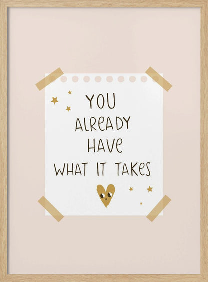 A motivational poster in a black frame with a pale pink background. A white piece of notebook paper is taped to the center with the handwritten text 'YOU ALREADY HAVE WHAT IT TAKES' in brown. It's decorated with small gold stars and a cute, smiling gold heart. Decor