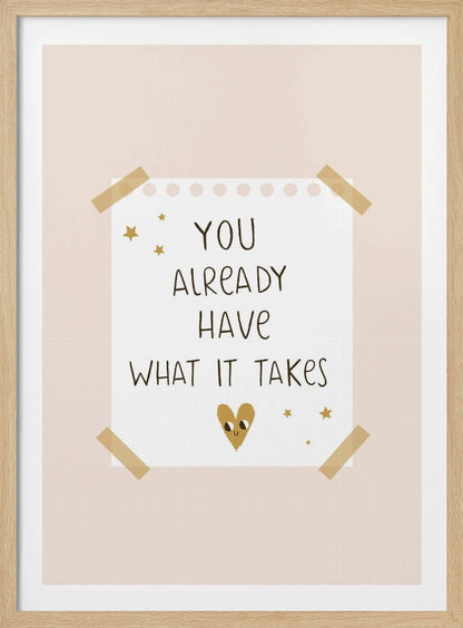 A motivational poster in a black frame with a pale pink background. A white piece of notebook paper is taped to the center with the handwritten text 'YOU ALREADY HAVE WHAT IT TAKES' in brown. It's decorated with small gold stars and a cute, smiling gold heart. Decor