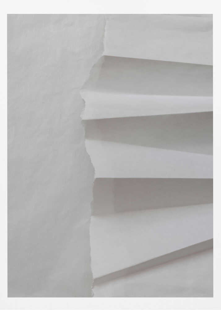 A minimalist composition of folded and torn white paper, showcasing geometric forms and shadows in a black frame.