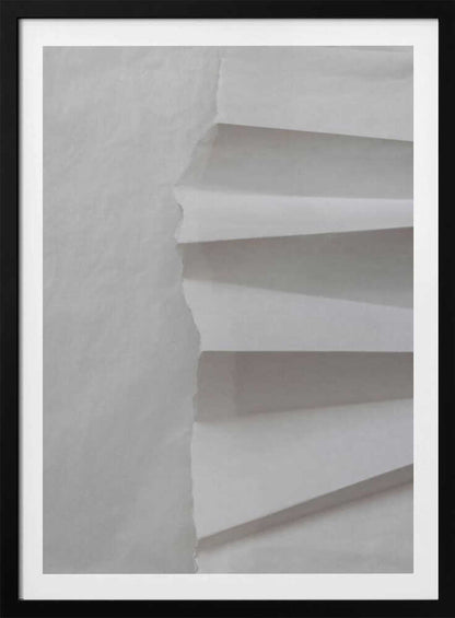 A minimalist composition of folded and torn white paper, showcasing geometric forms and shadows in a black frame.
