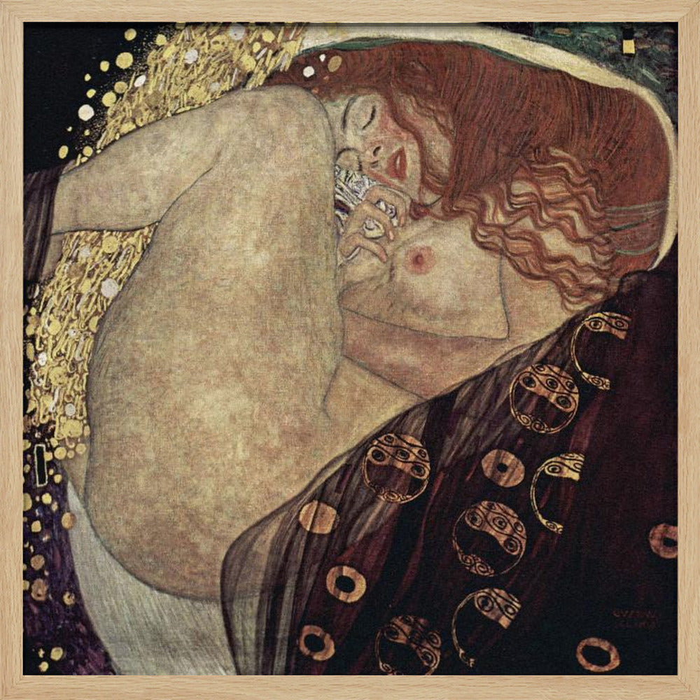 A print of Gustav Klimt's 1907 painting, 'Danaë'. The artwork depicts a sleeping, nude woman with vibrant red hair curled into a fetal position, receiving a shower of golden rain. The style is characteristic of Art Nouveau, with rich, decorative patterns on surrounding fabrics against a dark, star-like background, all within a light wood frame. Wall Art