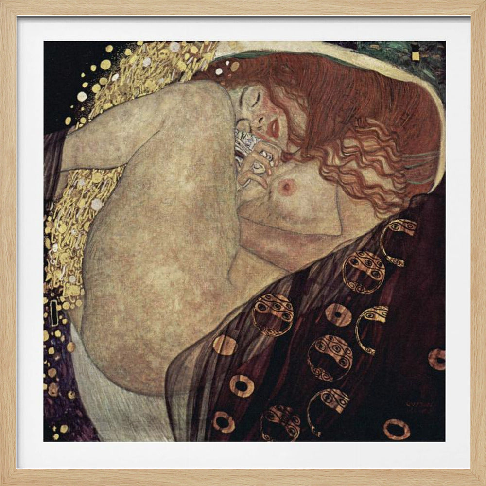 A print of Gustav Klimt's 1907 painting, 'Danaë'. The artwork depicts a sleeping, nude woman with vibrant red hair curled into a fetal position, receiving a shower of golden rain. The style is characteristic of Art Nouveau, with rich, decorative patterns on surrounding fabrics against a dark, star-like background, all within a light wood frame. Wall Art