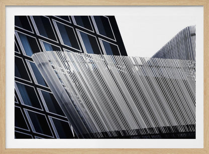 An abstract architectural photograph, framed in silver, showing a dynamic contrast between two modern building facades. In the background, a dark building features a grid of diamond-shaped windows with white frames, while a structure in the foreground creates a wave of fine, parallel white vertical lines against the sky and the other building. Print