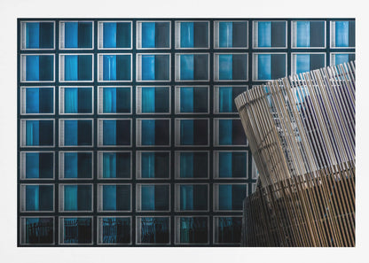 An architectural abstract photograph featuring a modern building facade with a grid of blue and black square windows, contrasted by a curved, slatted structure in the foreground, all enclosed in a silver frame. Wall Art