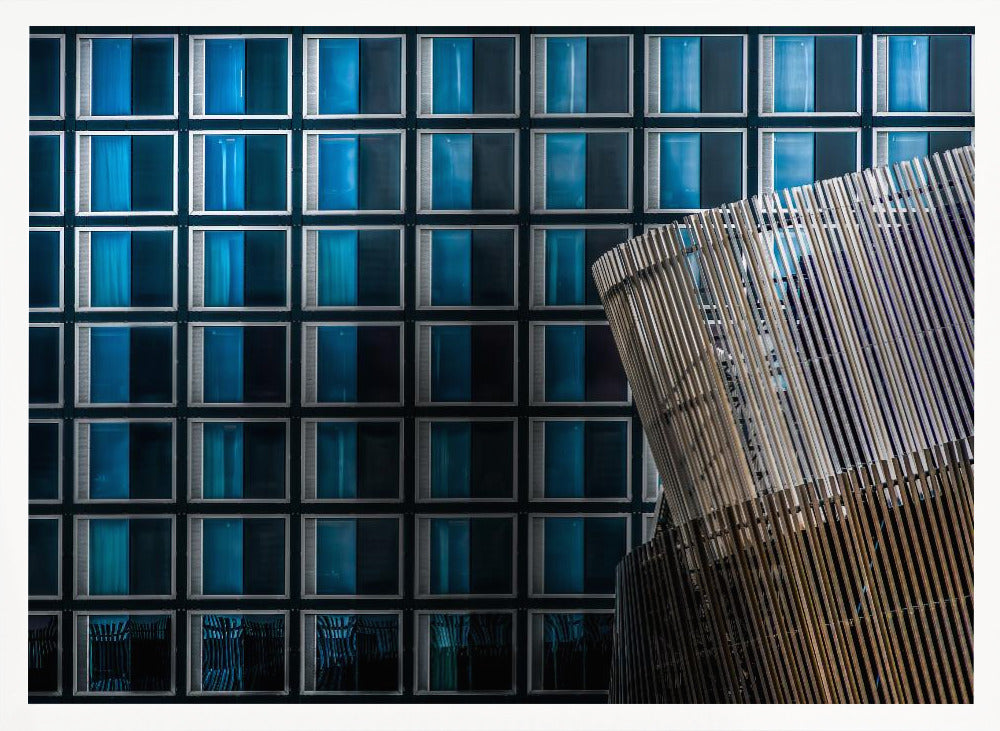 An architectural abstract photograph featuring a modern building facade with a grid of blue and black square windows, contrasted by a curved, slatted structure in the foreground, all enclosed in a silver frame. Wall Art