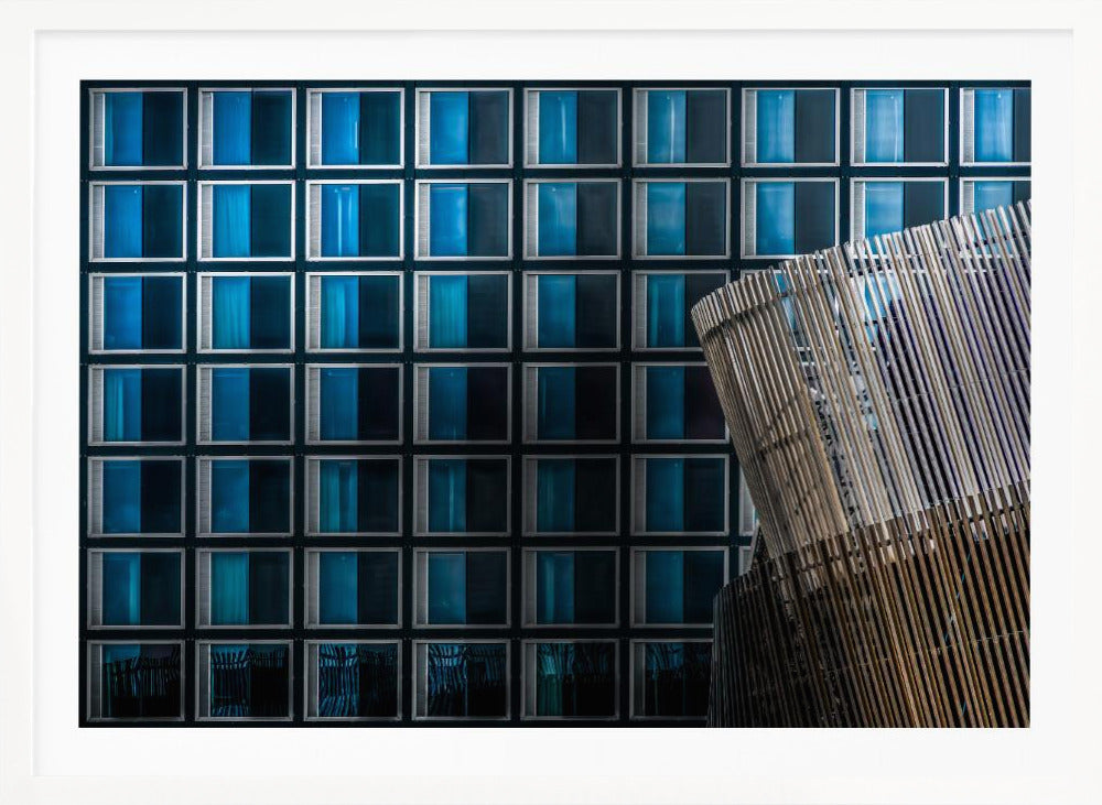 An architectural abstract photograph featuring a modern building facade with a grid of blue and black square windows, contrasted by a curved, slatted structure in the foreground, all enclosed in a silver frame. Wall Art