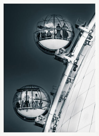A dramatic low-angle, black and white photograph of two spherical glass pods of the London Eye Ferris wheel. Silhouettes of people are visible inside the pods against a dark, solid sky, with the massive white structure of the wheel on the right. Print