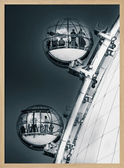 A dramatic low-angle, black and white photograph of two spherical glass pods of the London Eye Ferris wheel. Silhouettes of people are visible inside the pods against a dark, solid sky, with the massive white structure of the wheel on the right. Print
