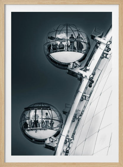 A dramatic low-angle, black and white photograph of two spherical glass pods of the London Eye Ferris wheel. Silhouettes of people are visible inside the pods against a dark, solid sky, with the massive white structure of the wheel on the right. Print