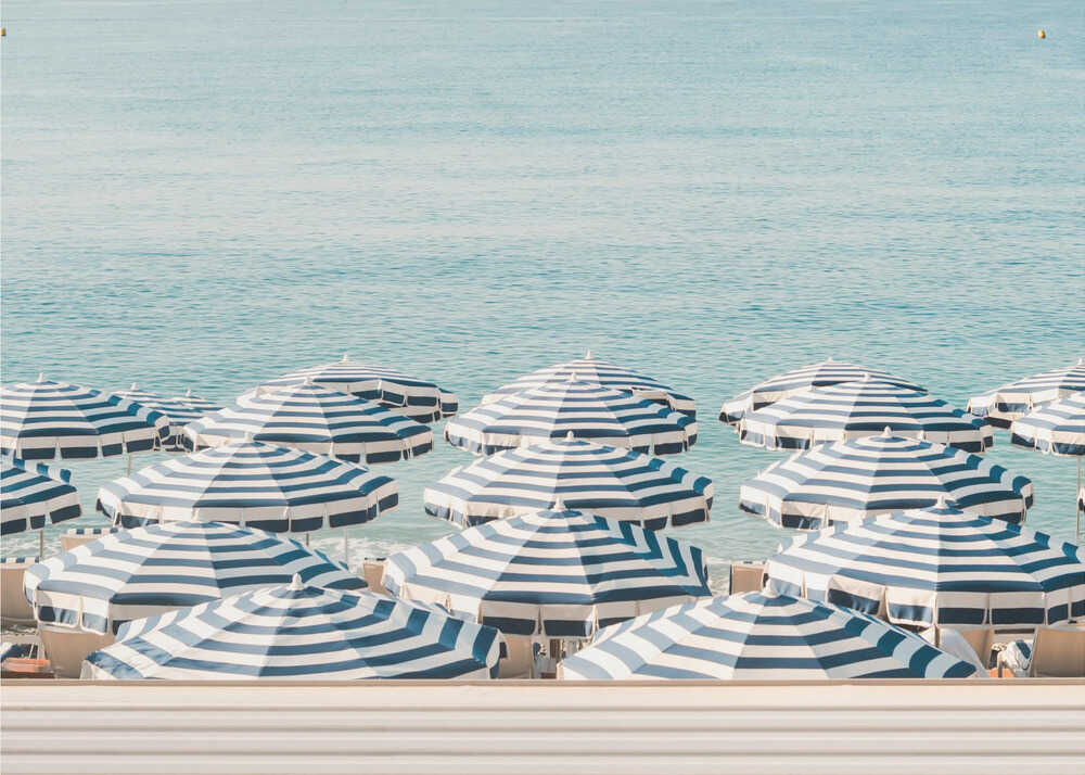 A serene beach scene viewed from above, featuring a multitude of blue and white striped umbrellas lining the shore in front of a calm, turquoise sea. Artwork