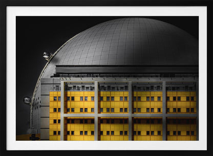 A framed architectural photograph with selective color, featuring a bright yellow building in the foreground against a monochrome background of a large grey dome structure under a black sky. Wall Art