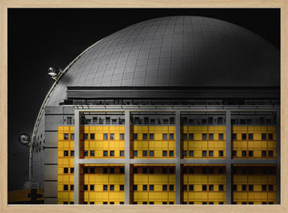 A framed architectural photograph with selective color, featuring a bright yellow building in the foreground against a monochrome background of a large grey dome structure under a black sky. Wall Art