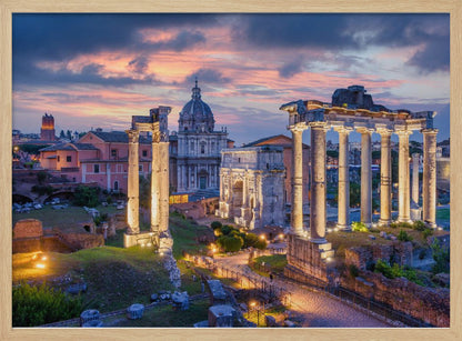 A scenic photograph of the ancient Roman Forum in Rome, Italy, at dusk. The ruins, including prominent columns and arches, are illuminated by warm lights, contrasting with the deep blue and vibrant pink of the sunset sky. Wall Art