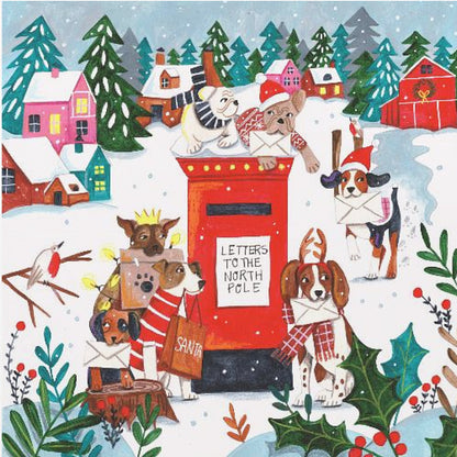 A whimsical Christmas illustration of several dogs in festive hats and scarves mailing letters at a bright red postbox labeled 'Letters to the North Pole' in a snowy village scene with colorful houses and pine trees. Decor