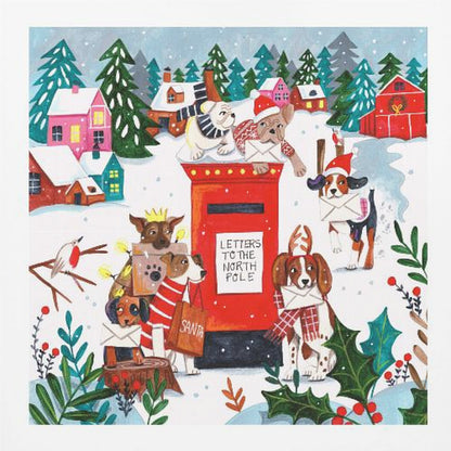 A whimsical Christmas illustration of several dogs in festive hats and scarves mailing letters at a bright red postbox labeled 'Letters to the North Pole' in a snowy village scene with colorful houses and pine trees. Decor