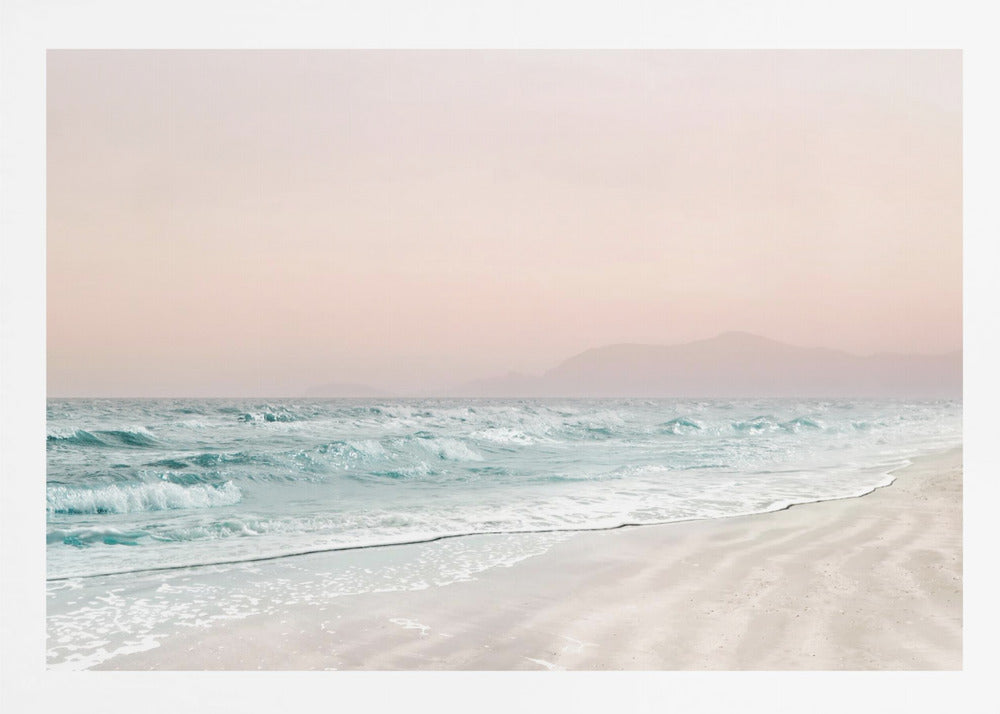 A serene coastal scene with gentle turquoise waves washing onto a sandy beach. The sky is a soft, hazy pink, and faint outlines of mountains are visible in the distant background. The artwork is presented in a silver frame. Print