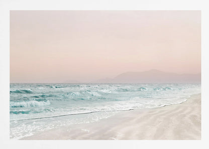 A serene coastal scene with gentle turquoise waves washing onto a sandy beach. The sky is a soft, hazy pink, and faint outlines of mountains are visible in the distant background. The artwork is presented in a silver frame. Print