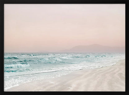 A serene coastal scene with gentle turquoise waves washing onto a sandy beach. The sky is a soft, hazy pink, and faint outlines of mountains are visible in the distant background. The artwork is presented in a silver frame. Print