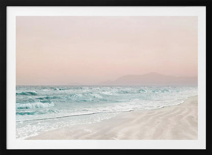 A serene coastal scene with gentle turquoise waves washing onto a sandy beach. The sky is a soft, hazy pink, and faint outlines of mountains are visible in the distant background. The artwork is presented in a silver frame. Print