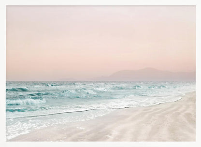 A serene coastal scene with gentle turquoise waves washing onto a sandy beach. The sky is a soft, hazy pink, and faint outlines of mountains are visible in the distant background. The artwork is presented in a silver frame. Print
